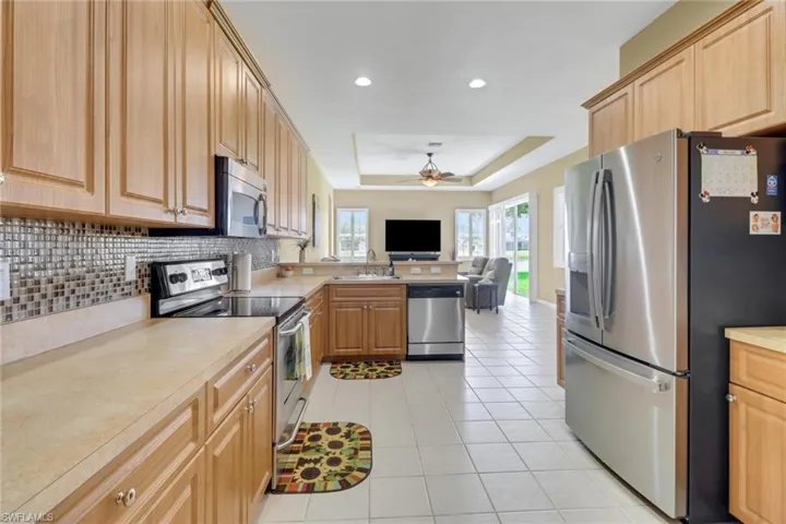 Kitchen featuring stainless steel appliances, a sink, open floor plan, a tray ceiling, and ceiling fan