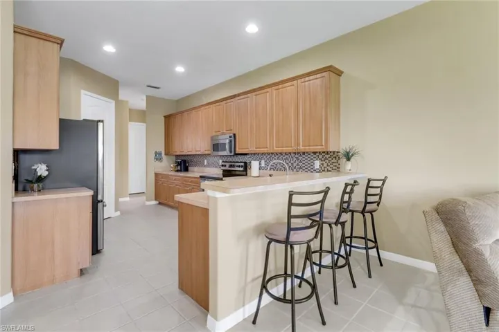 Kitchen featuring stainless steel appliances, a peninsula, a breakfast bar area, decorative backsplash, and baseboards