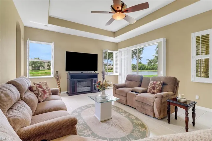 Living room featuring light tile patterned floors, a tray ceiling, baseboards, and a ceiling fan