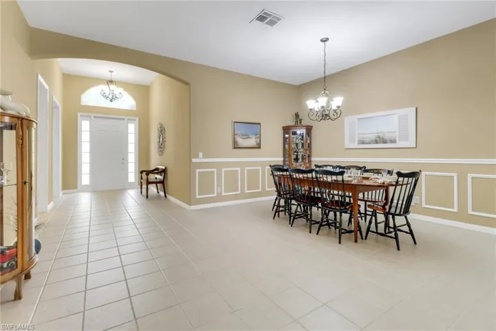 Dining space with a chandelier, arched walkways, a decorative wall, light tile patterned floors, and a wainscoted wall