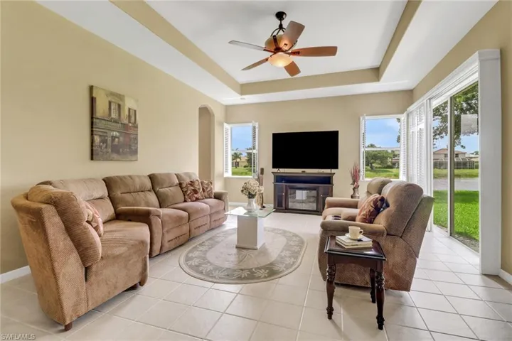 Living room with a raised ceiling, arched walkways, ceiling fan, light tile patterned floors, and baseboards