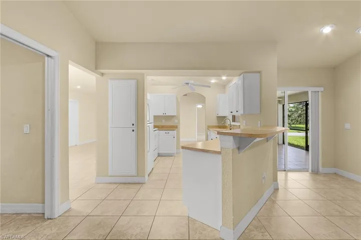 Kitchen featuring white cabinets, a breakfast bar, kitchen peninsula, light tile patterned flooring, and ceiling fan