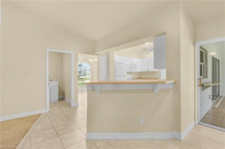 Kitchen with a kitchen bar, white appliances, kitchen peninsula, light tile patterned flooring, and white cabinetry