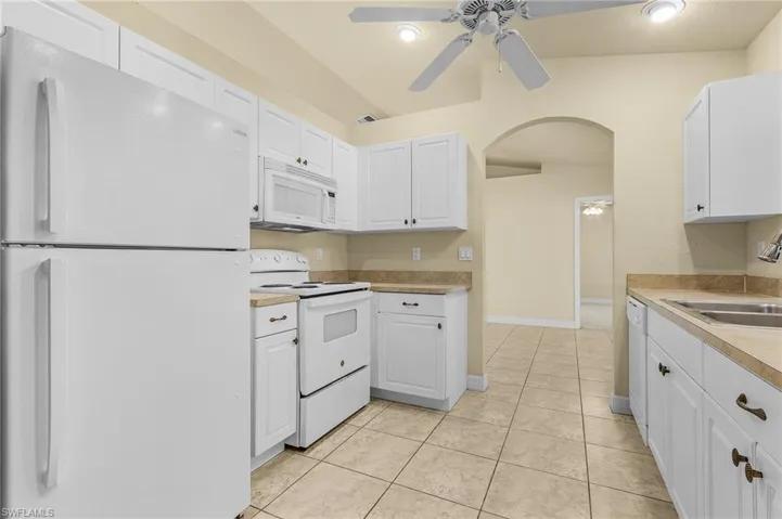Kitchen featuring white appliances, white cabinets, sink, light tile patterned floors, and ceiling fan