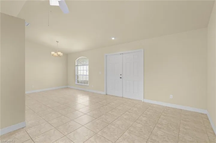 Spare room featuring lofted ceiling, ceiling fan with notable chandelier, and light tile patterned floors