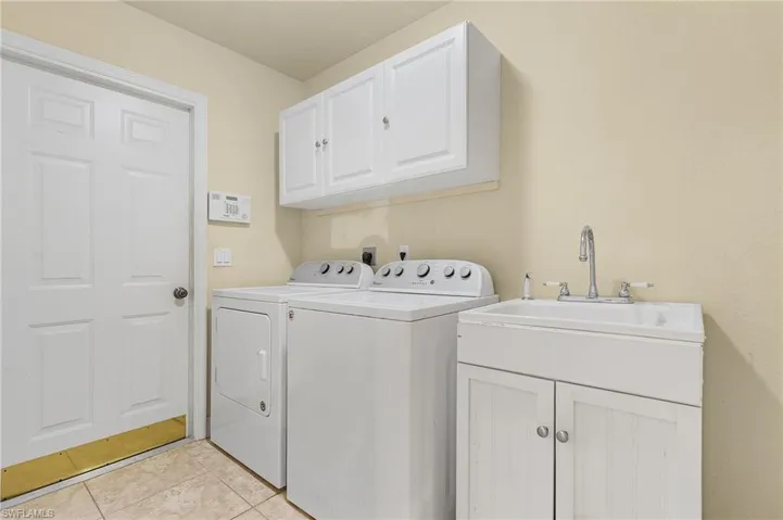 Laundry area with sink, separate washer and dryer, cabinets, and light tile patterned floors