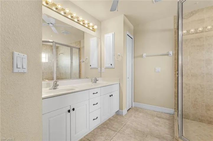 Bathroom featuring tile patterned flooring, double sink vanity, a shower with door, and ceiling fan