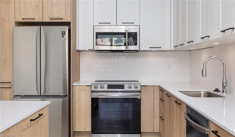 Kitchen with light brown cabinets, a sink, light countertops, appliances with stainless steel finishes, and decorative backsplash