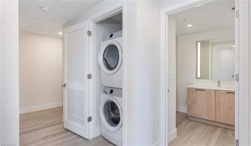 Clothes washing area featuring baseboards, laundry area, stacked washer and dryer, recessed lighting, and light wood-style flooring