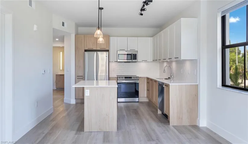 Kitchen with baseboards, a sink, appliances with stainless steel finishes, decorative backsplash, and a kitchen island