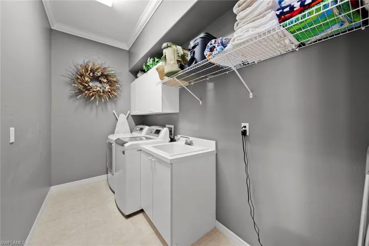 Laundry area featuring independent washer and dryer, light tile flooring, crown molding, hookup for a washing machine, and sink
