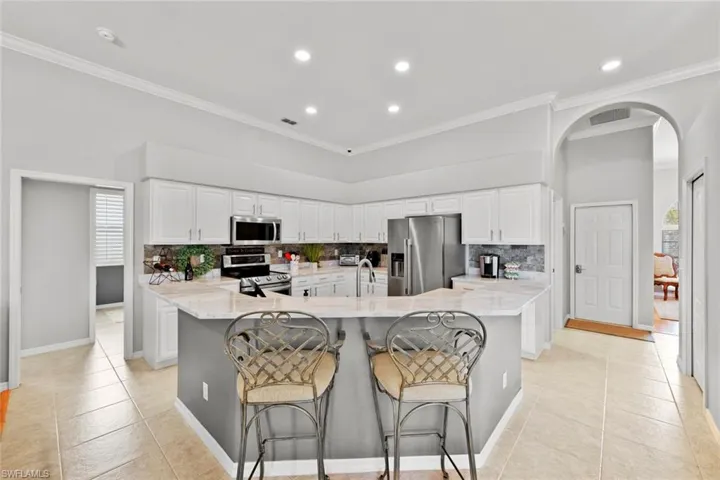 Kitchen with white cabinetry, stainless steel appliances, a kitchen bar, tas