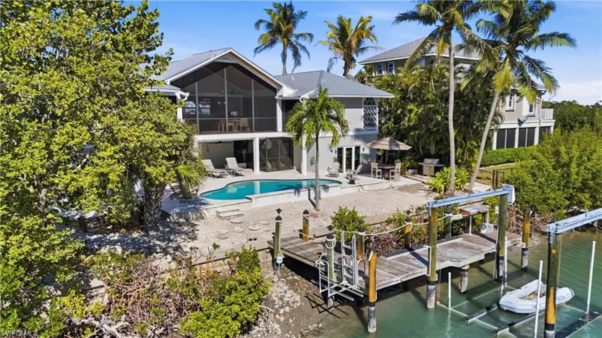 Back of house with boat lift, a sunroom, an outdoor pool, a patio, and a metal roof - Virtually Edited Image