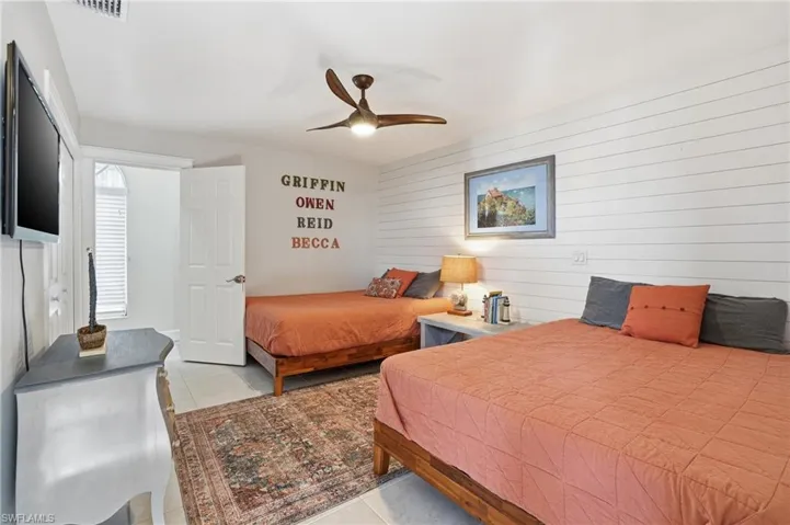 Bedroom featuring wooden walls, a ceiling fan, light tile patterned floors, and an accent wall - Virtually Edited Image