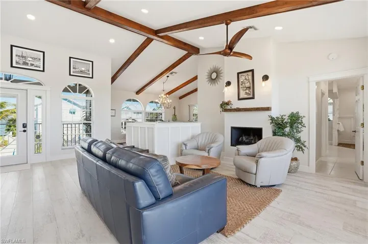 Living room with beamed ceiling, a fireplace, a chandelier, high vaulted ceiling, and light wood-type flooring - Virtually Edited Image