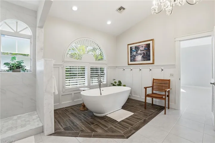 Bathroom with wainscoting, a freestanding bath, a decorative wall, a walk in shower, and lofted ceiling - Virtually Edited Image