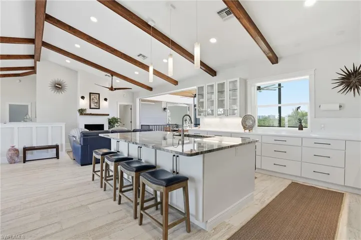 Kitchen featuring white cabinets, a kitchen island with sink, glass insert cabinets, recessed lighting, and a breakfast bar - Virtually Edited Image