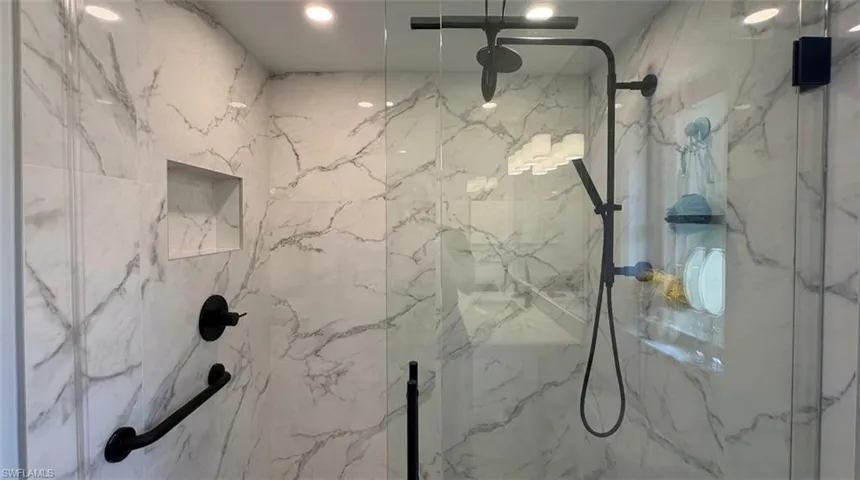 Walk-in shower with clear glass enclosure, a matte black rain shower head, hand-held sprayer, built-in niche, and white marble-look wall tiling