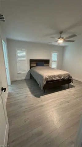 Light wood-finish flooring, white walls, and a ceiling fan with integrated lighting