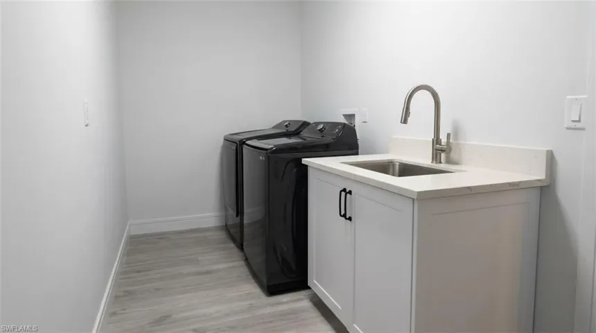 Wood-finish flooring, white cabinetry with black hardware, stainless steel sink, and light-toned countertop