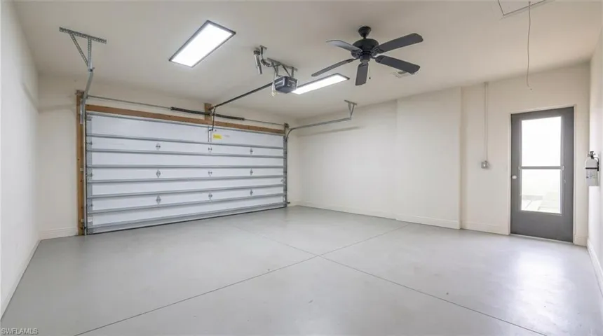 Spacious garage with a sectional overhead door, concrete flooring, ceiling fan, and fluorescent lighting