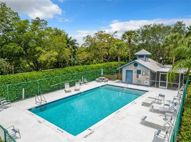 Outdoor swimming pool with concrete decking, surrounding green fencing, and a pool house featuring a screened porch