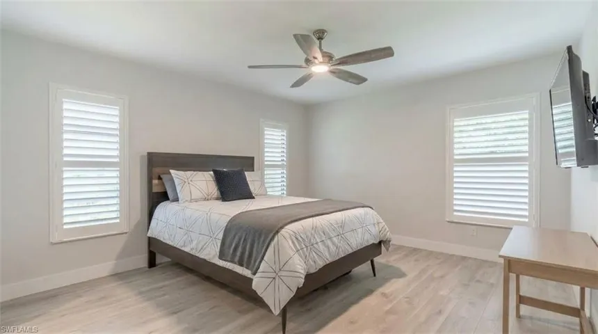 Light wood-finish flooring, two windows with white plantation shutters, and a ceiling fan with integrated lighting
