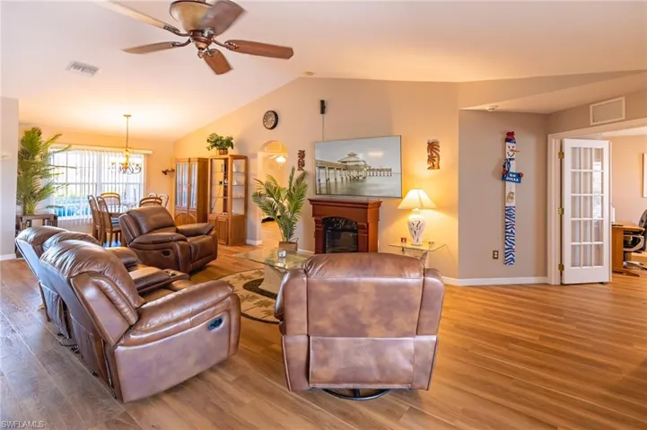 Living room with hardwood / wood-style flooring, ceiling fan with notable chandelier, and vaulted ceiling