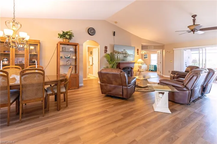 Living room featuring ceiling fan with notable chandelier, wood-type flooring, and vaulted ceiling