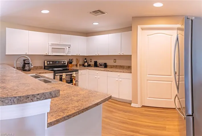 Kitchen featuring kitchen peninsula, appliances with stainless steel finishes, sink, white cabinets, and light hardwood / wood-style floors