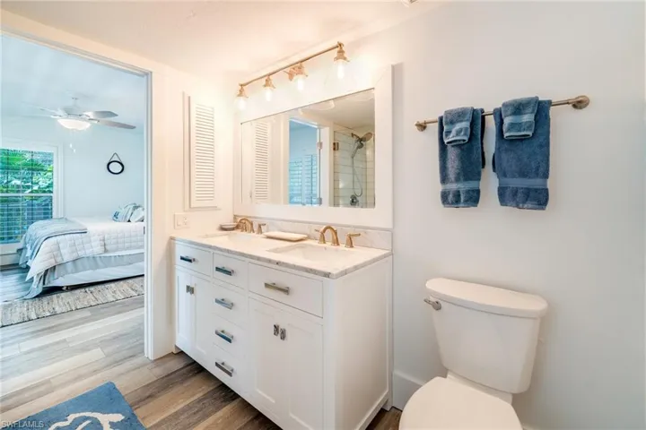 Ensuite bathroom with double vanity, light wood-style floors, tiled shower, and ceiling fan