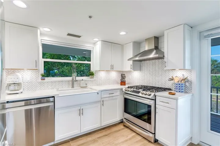 Kitchen with plenty of natural light, stainless steel appliances, white cabinets, wall chimney range hood, and recessed lighting