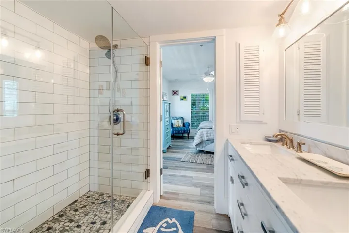 Ensuite bathroom featuring double vanity, a stall shower, and light wood-style floors
