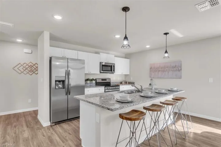 Kitchen featuring stainless steel appliances, white cabinetry, light stone countertops, sink, and light hardwood / wood-style floors