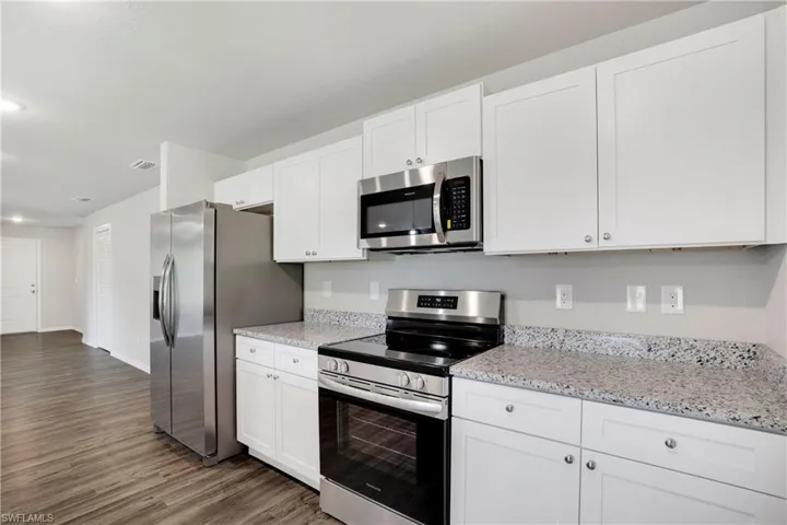 Kitchen with light stone counters, appliances with stainless steel finishes, dark hardwood / wood-style floors, and white cabinets