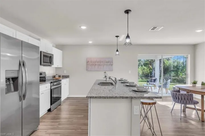 Kitchen with white cabinetry, a center island with sink, decorative light fixtures, and appliances with stainless steel finishes