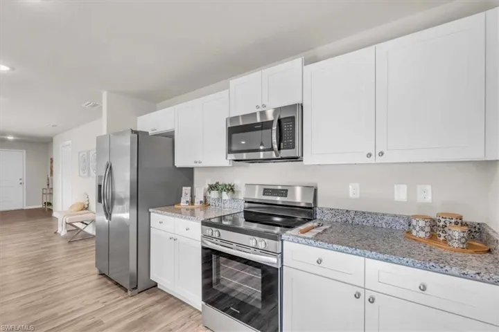 Kitchen featuring light hardwood / wood-style flooring, white cabinets, light stone counters, and stainless steel appliances