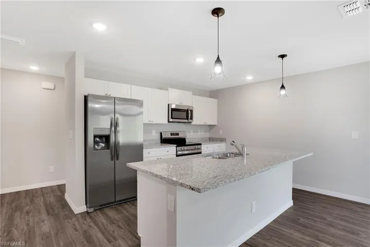 Kitchen with appliances with stainless steel finishes, sink, decorative light fixtures, dark wood-type flooring, and a kitchen island with sink