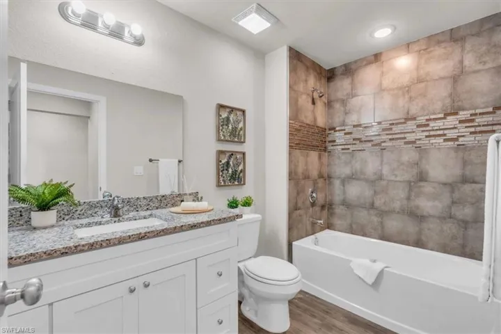 Full bathroom with toilet, vanity, tiled shower / bath, and wood-type flooring
