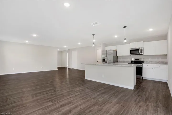 Kitchen featuring an island with sink, stainless steel appliances, decorative light fixtures, white cabinets