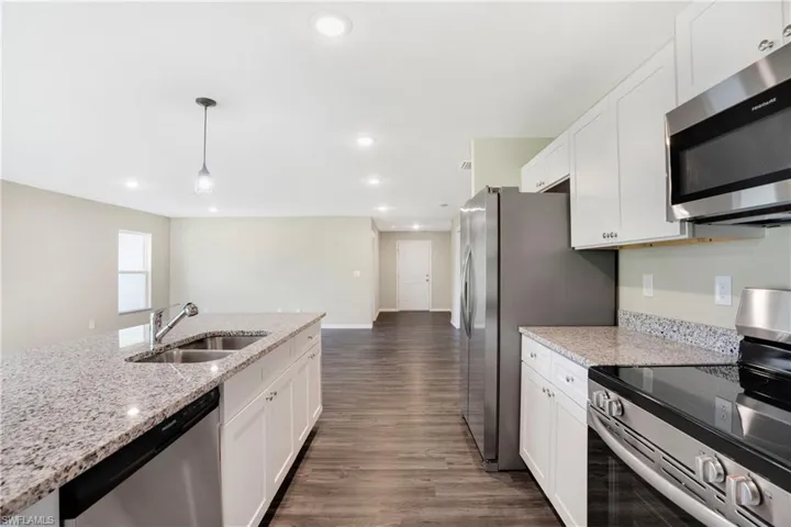 Kitchen with light stone counters, appliances with stainless steel finishes, decorative light fixtures