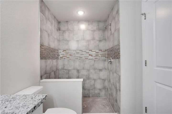 En-suite Bathroom with a tile shower, a textured ceiling, toilet, and vanity