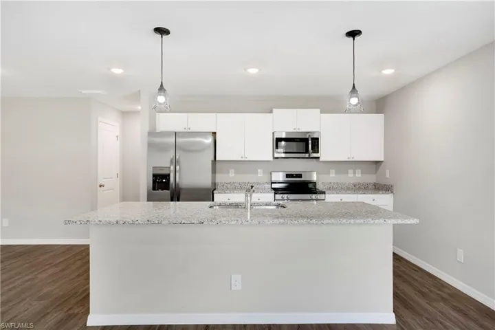 Kitchen featuring hanging light fixtures, a kitchen island with sink, dark wood-type flooring, sink, and stainless steel appliances