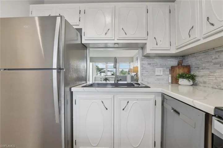 Kitchen featuring stainless steel appliances, white cabinets, tasteful backsplash, and light countertops