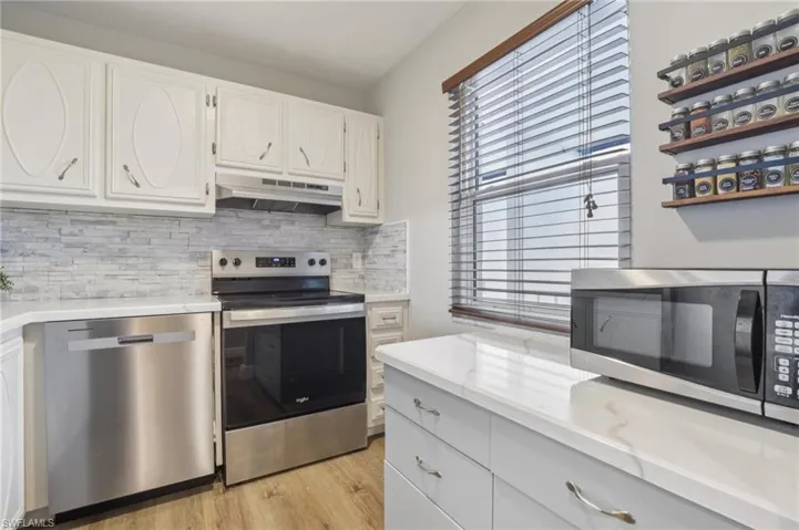 Kitchen with appliances with stainless steel finishes, decorative backsplash, white cabinets, under cabinet range hood, and light wood-style floors