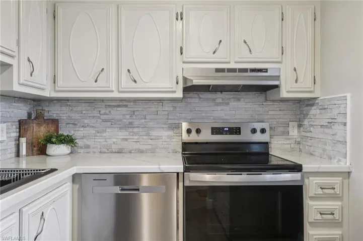 Kitchen with appliances with stainless steel finishes, backsplash, white cabinets, and under cabinet range hood