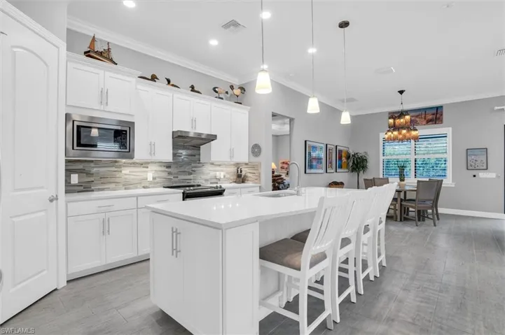 Kitchen featuring stainless steel microwave, a sink, range with electric stovetop, under cabinet range hood, and tasteful backsplash
