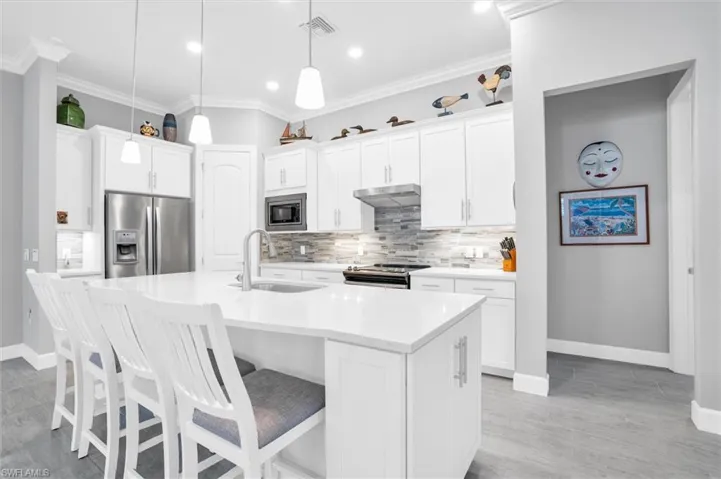 Kitchen featuring appliances with stainless steel finishes, a sink, under cabinet range hood, backsplash, and baseboards