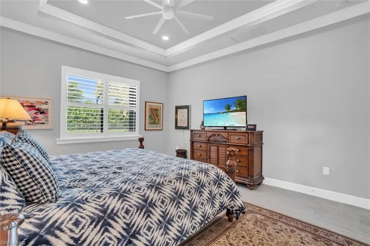 Bedroom featuring a tray ceiling, crown molding, recessed lighting, ceiling fan, and baseboards