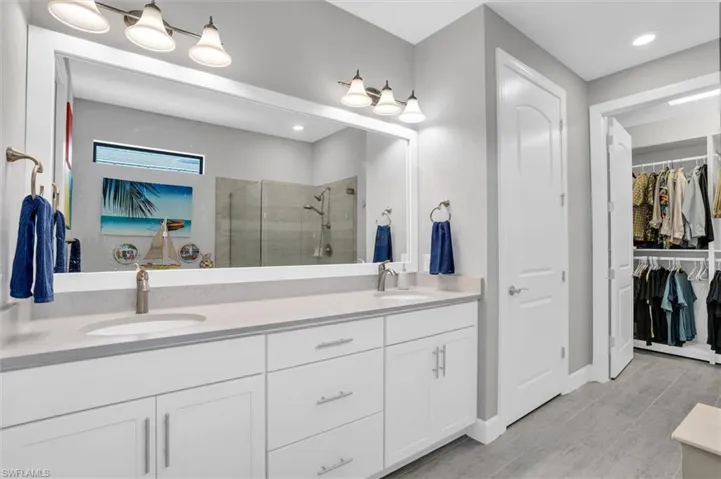 Full bathroom featuring a stall shower, double vanity, a walk in closet, and baseboards
